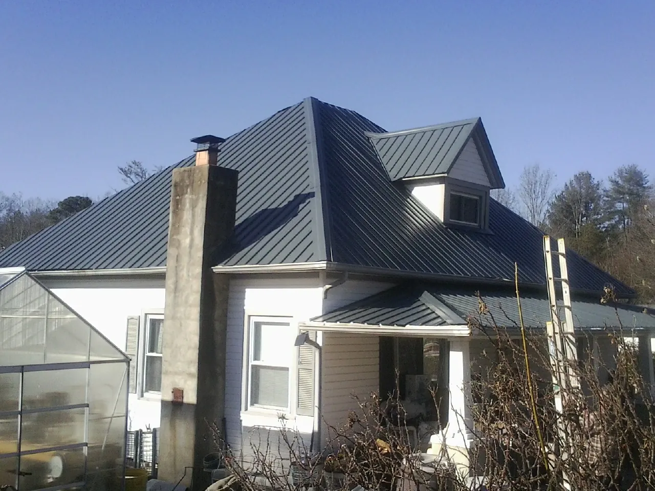 Dark blue standing seam metal roof on a white farmhouse with dormer — Slate & Tile Roof Repair by Roofing Brothers in Ogden